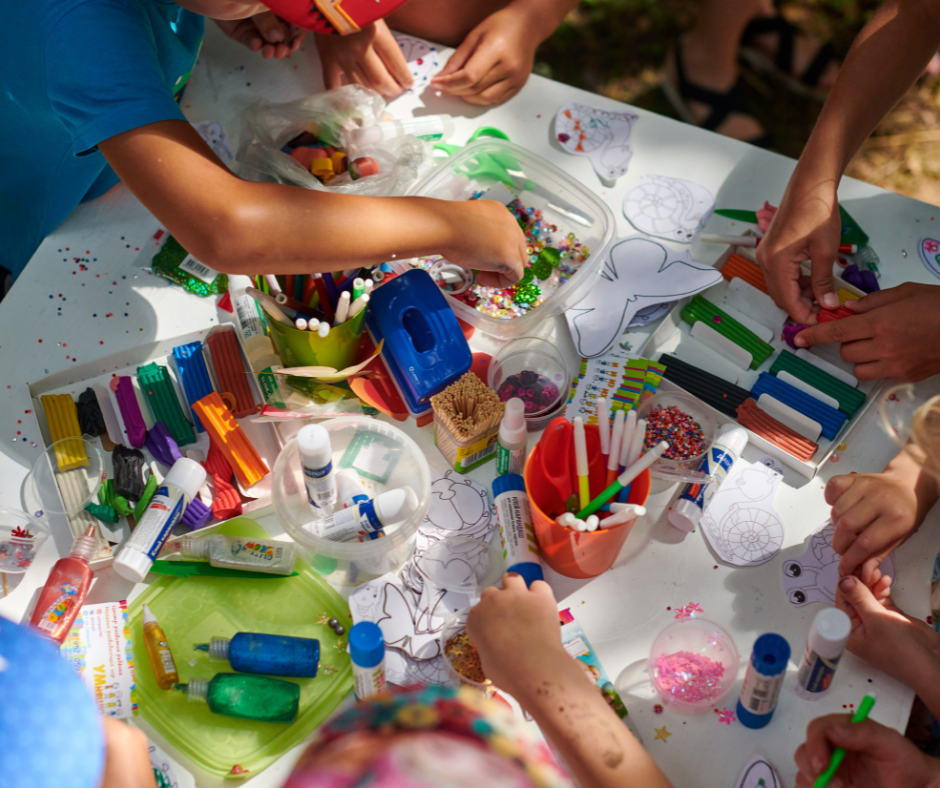 Website Value Creativity A large number of crafting supplies are on a table, being used by children to create art.